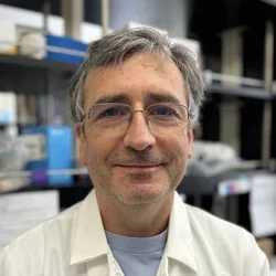 Giancarlo Costaguta wearing a lab coat and standing in a laboratory.